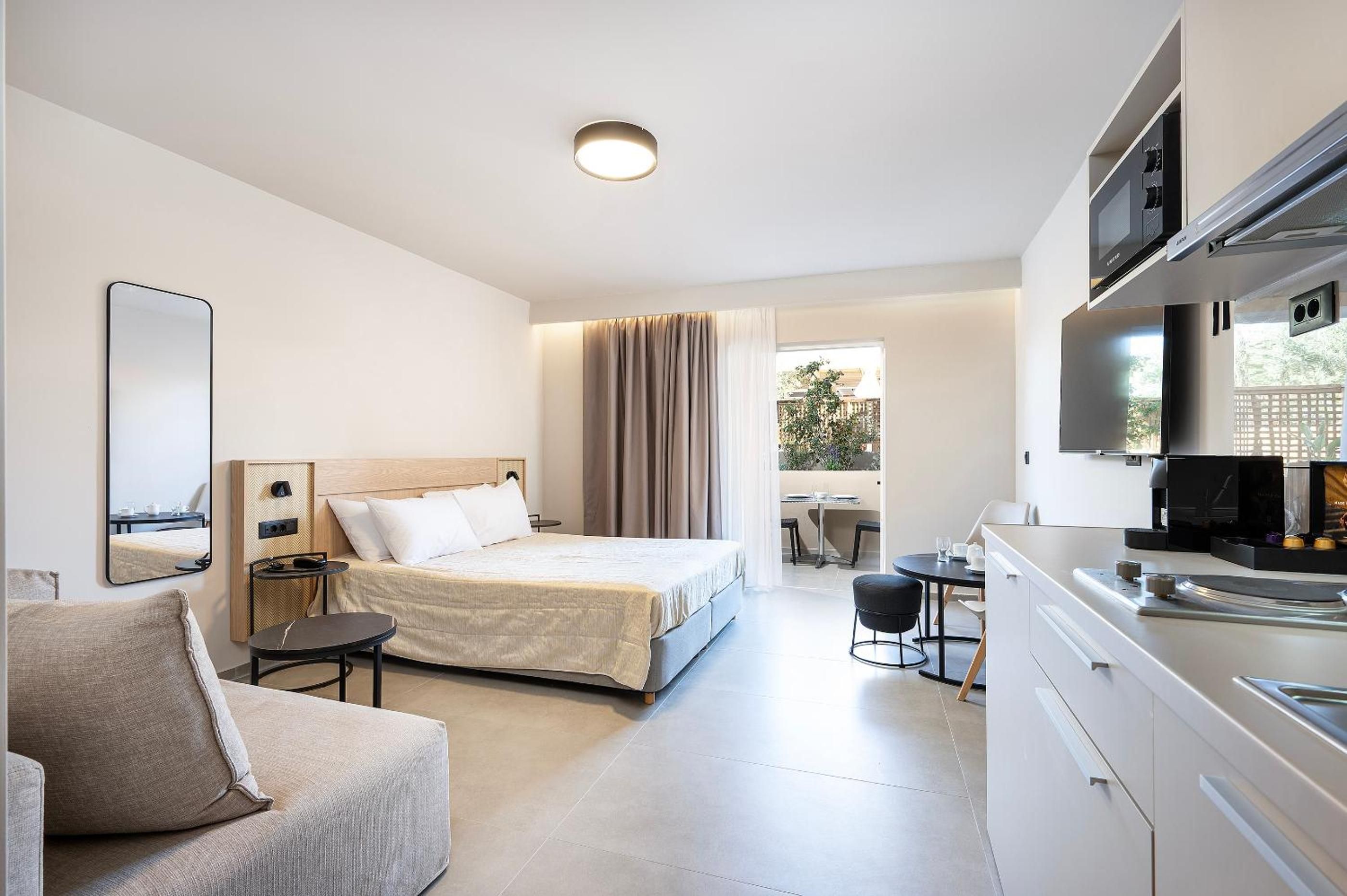 Ein modernes Hotelzimmer mit Bett, einer Couch, einem Esstisch und einer Küchenzeile.