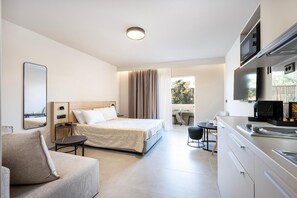 Habitació d'hotel moderna amb llit, sofà, taula de dinar i petita cuina.