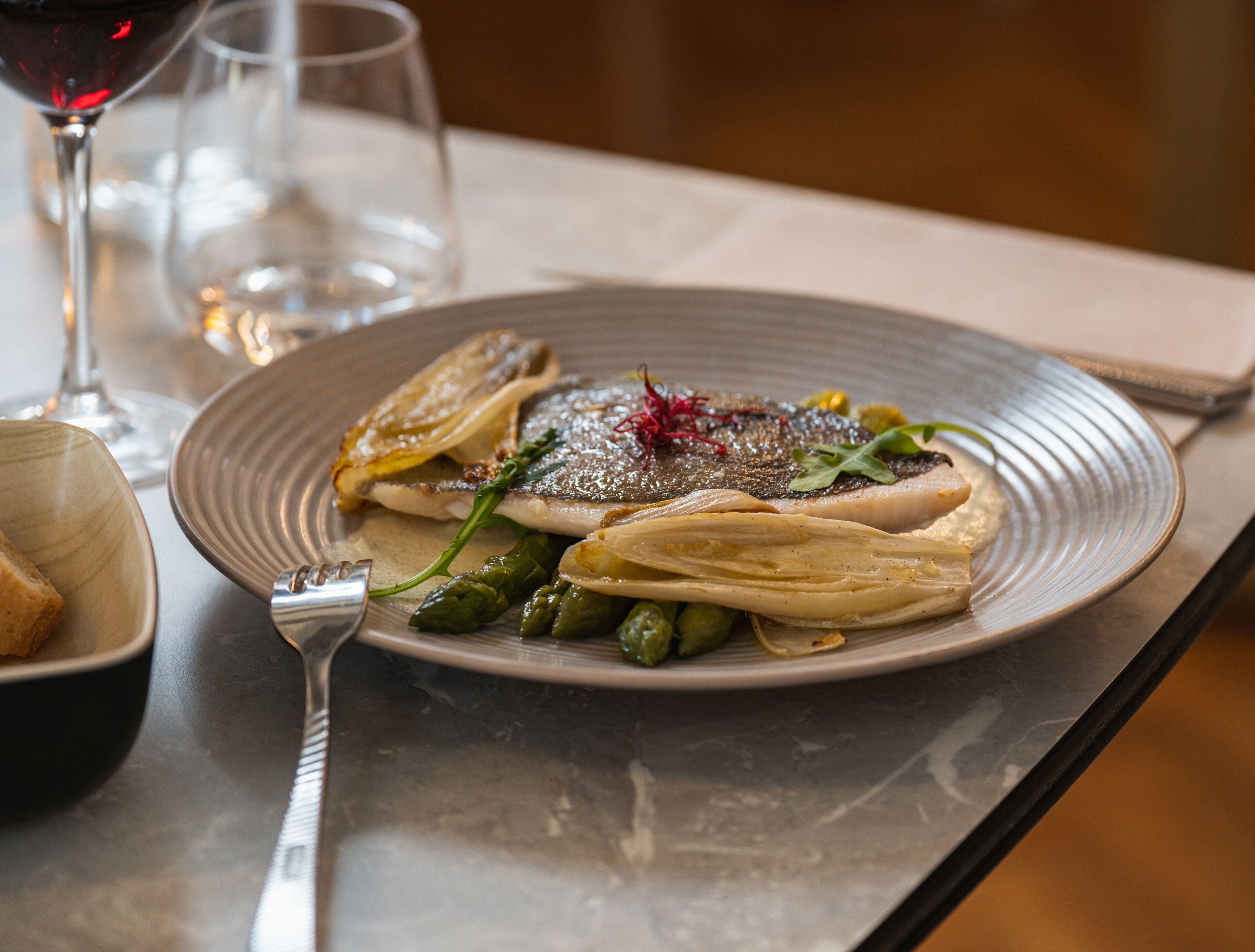 A plate of food with a fork and a glass of red wine on a table.