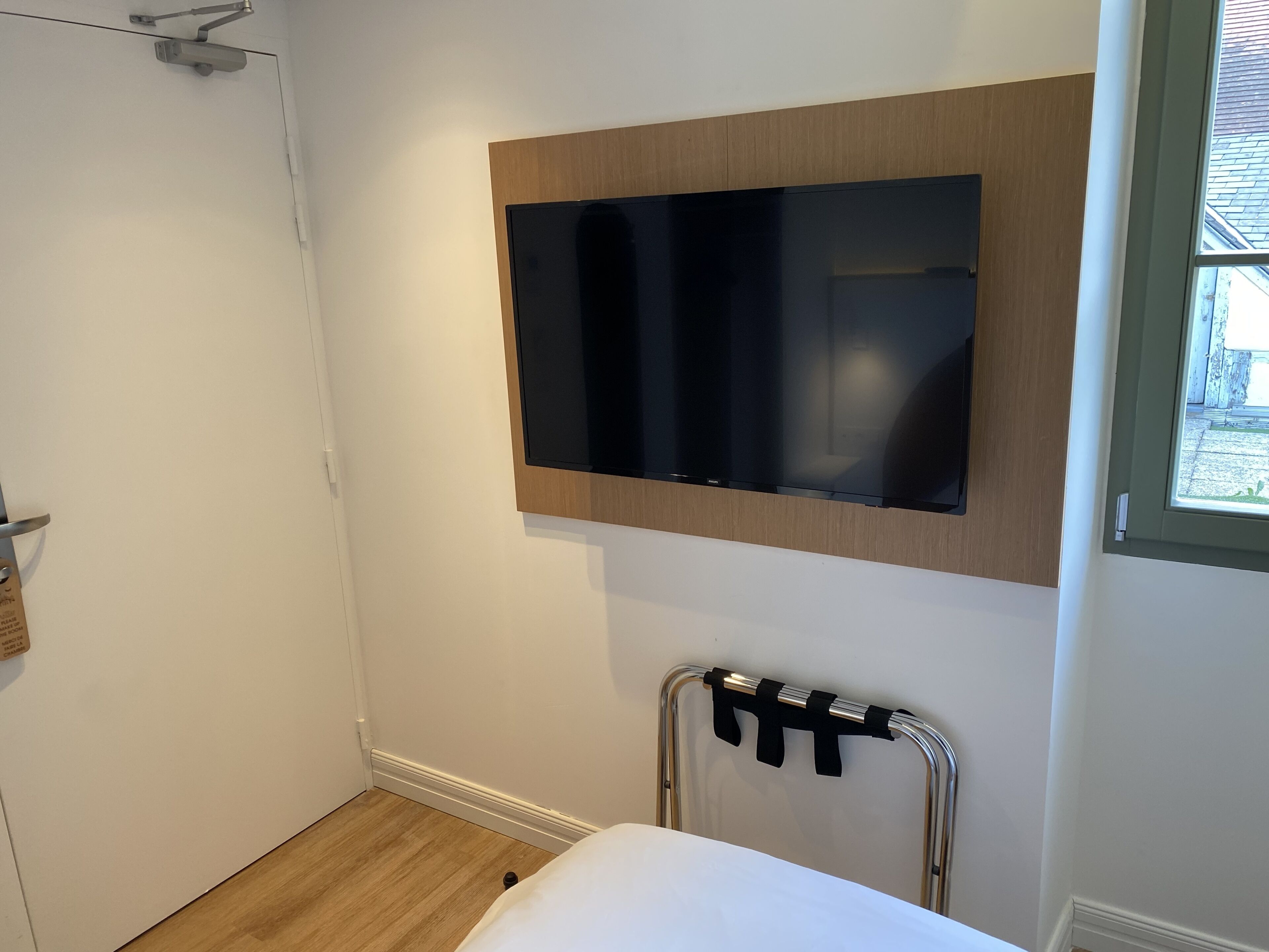 Ett sovrum med en väggmonterad TV, en säng, en stol och ett fönster.