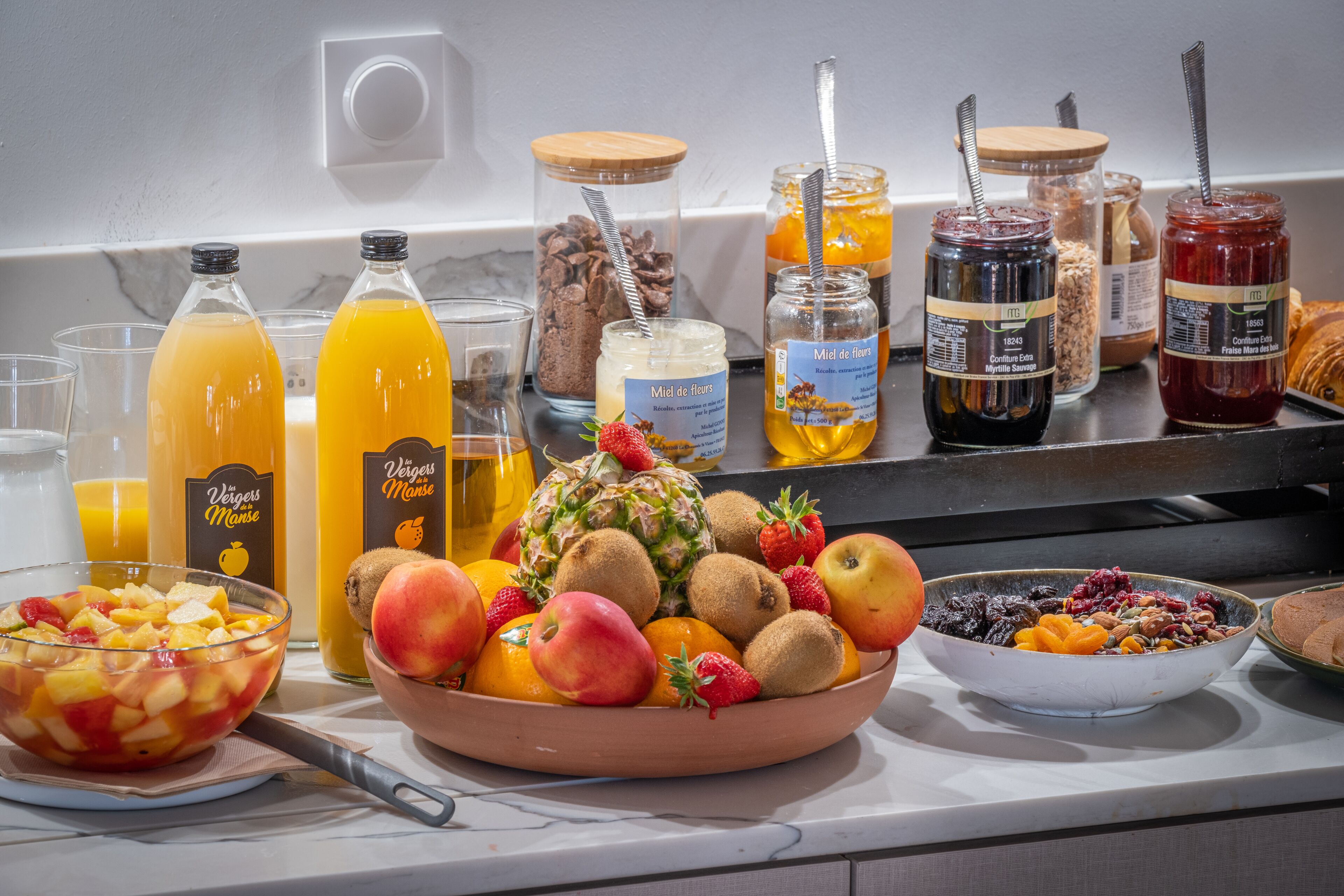 En frukostbuffé med ett urval av olika frukter, juicer och marmelader.