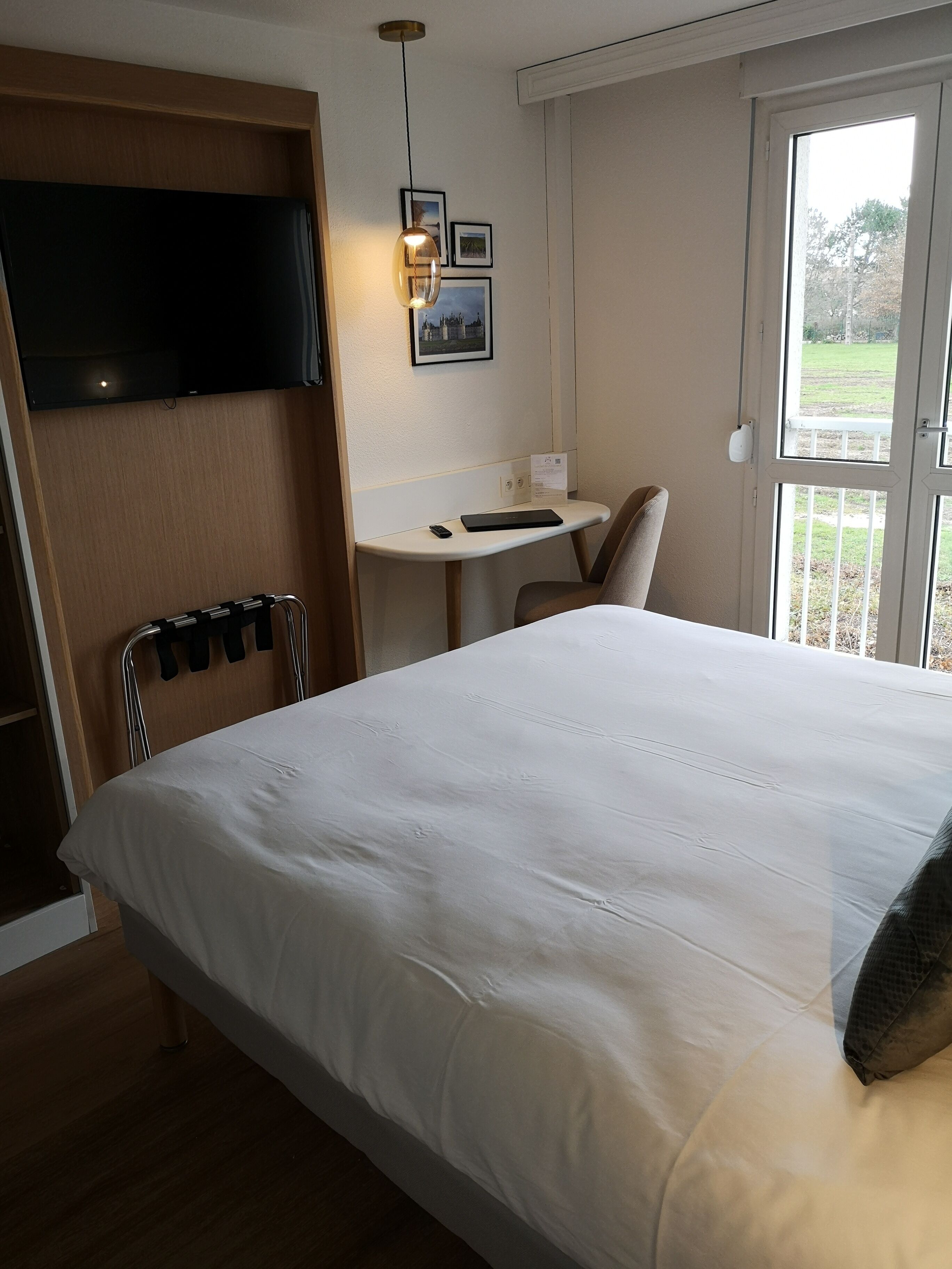 Una habitación de hotel con cama, escritorio, silla y televisor montado en la pared.