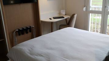 Una habitación de hotel con cama, escritorio, silla y televisor montado en la pared.