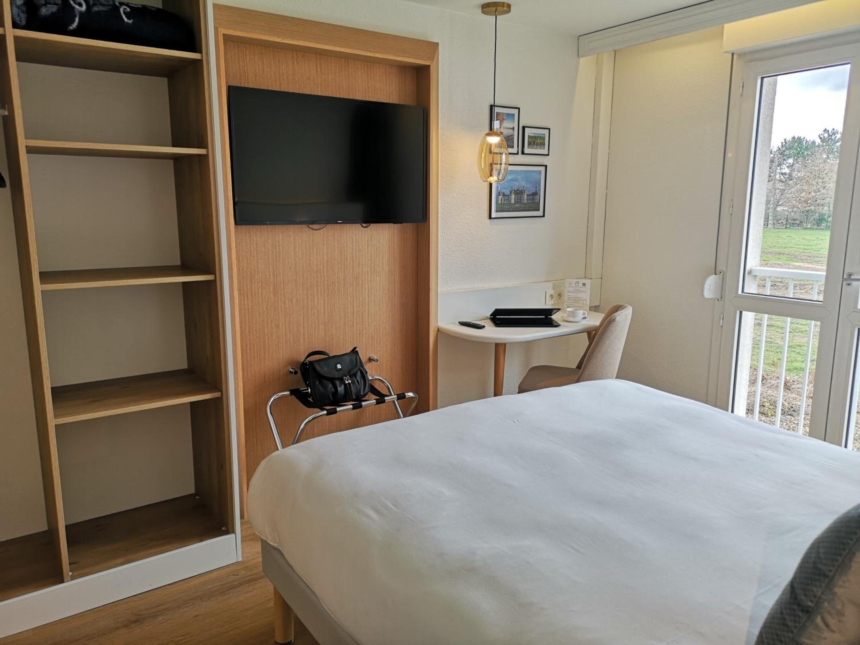 Habitació d'hotel amb llit, escriptori, cadira, televisió i armari.