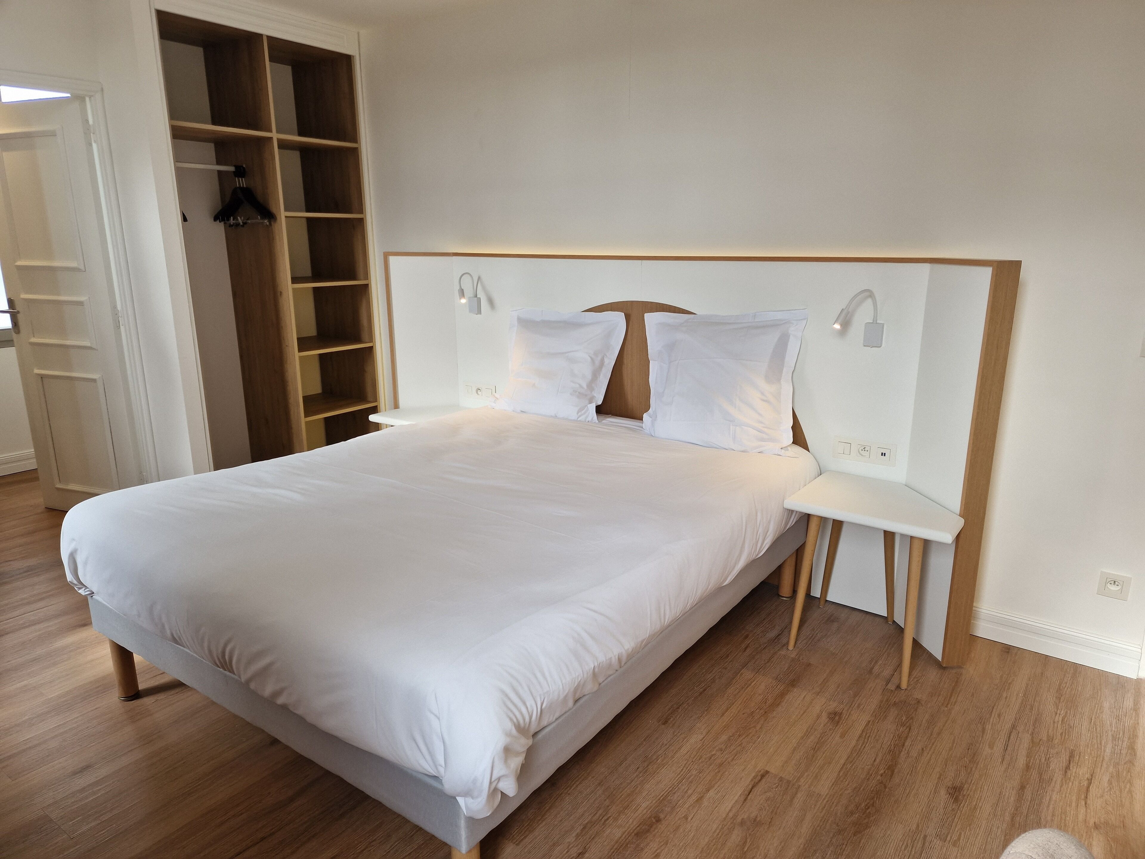 Un lit bien fait, avec une tête de lit en bois, une table de chevet et une armoire intégrée dotée de plusieurs étagères.