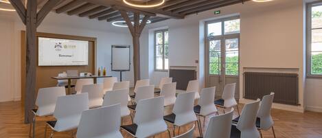 A conference room with white chairs arranged in rows, a wooden ceiling, and a presentation screen displaying a welcome message.