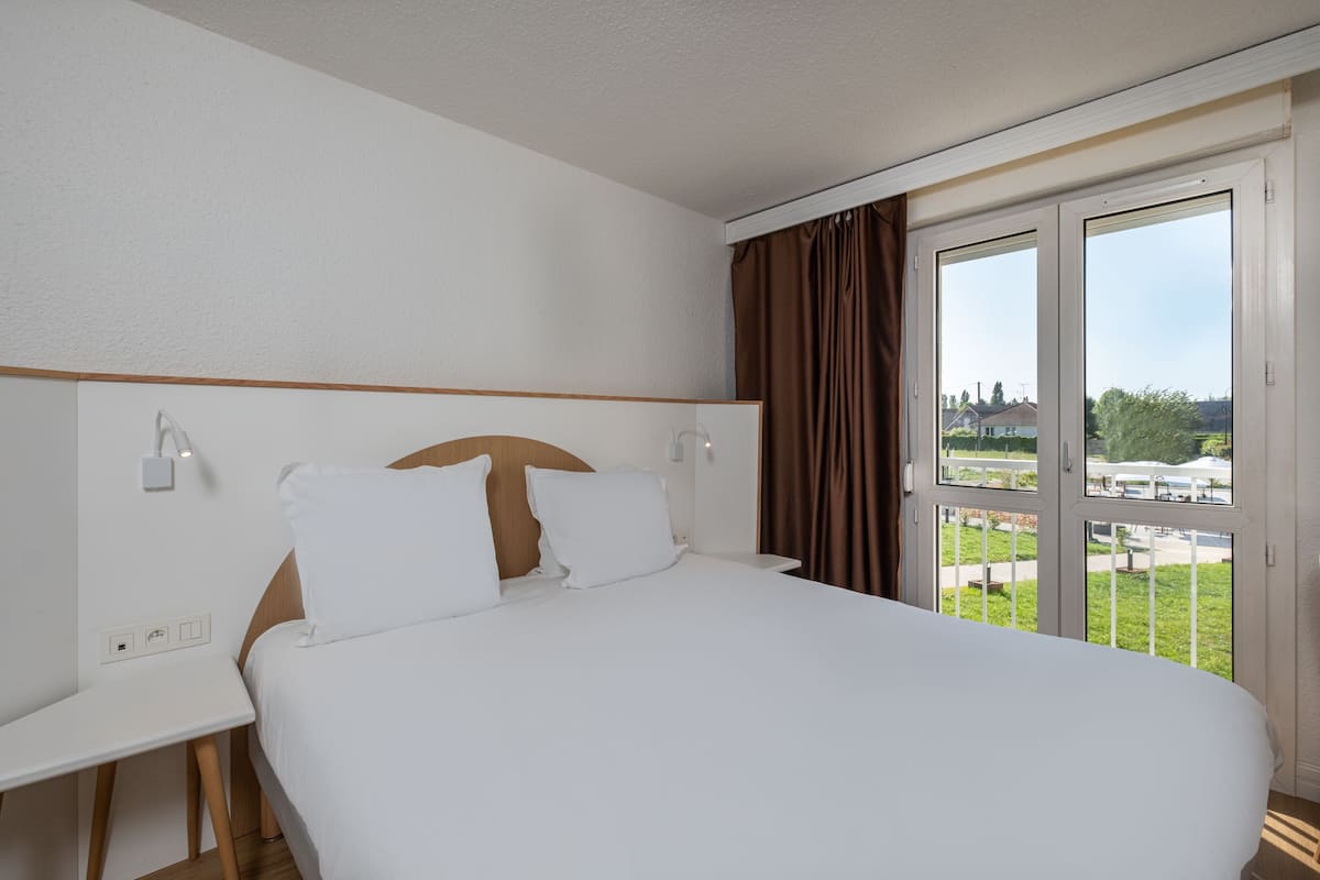 A hotel room with a large bed, a desk, and a window with curtains.