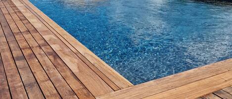 A wooden deck surrounding a clear blue pool with a wooden cabin in the background.
