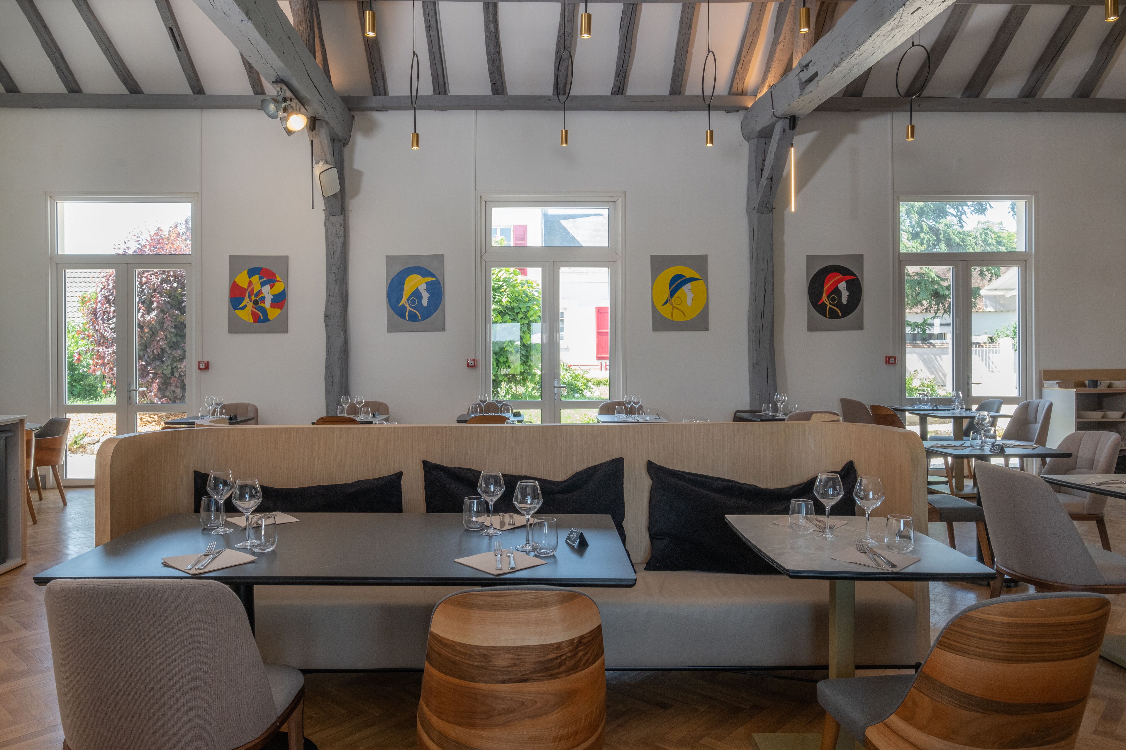 A modern restaurant with a long wooden bench seating area, tables with chairs, and artwork on the walls.