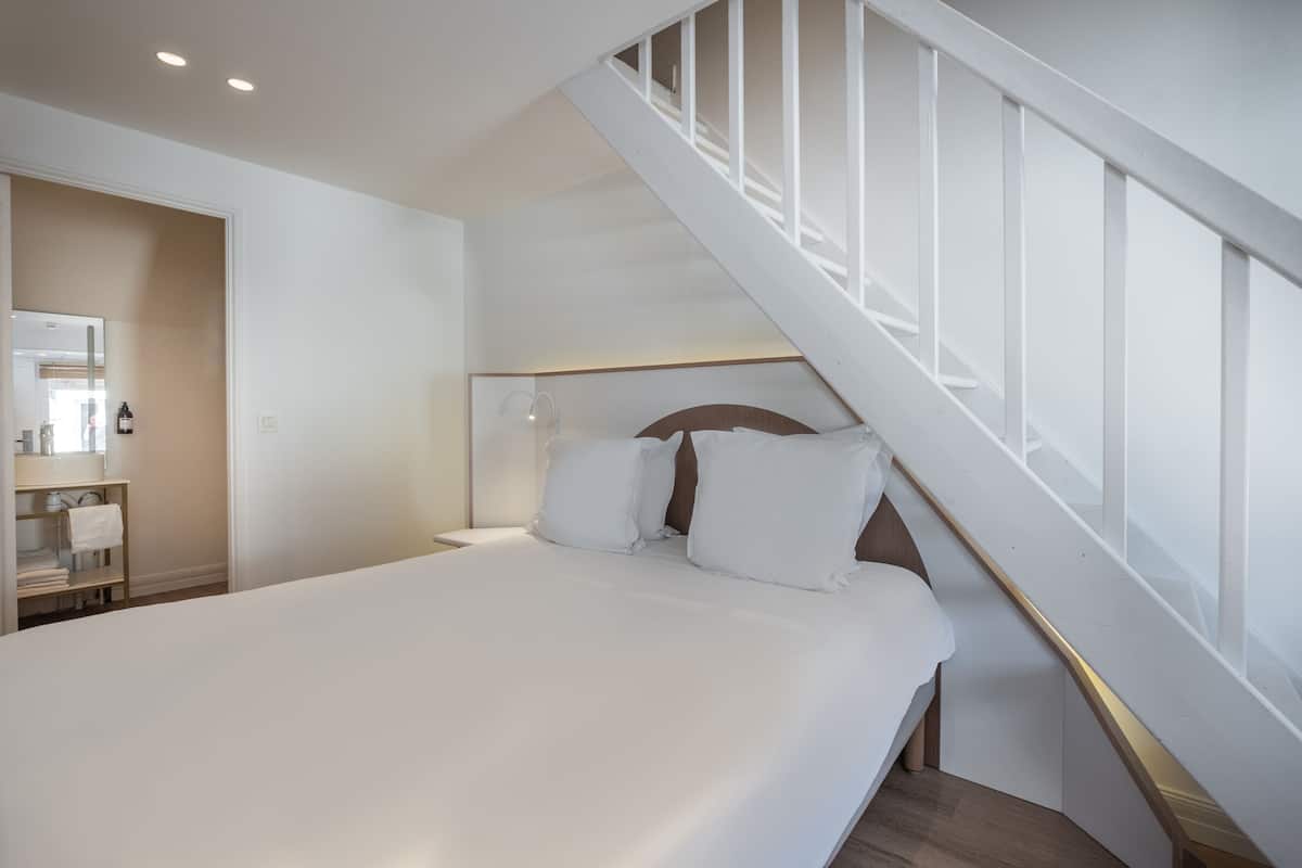 A bedroom with a large bed, a wooden headboard, and a white staircase.