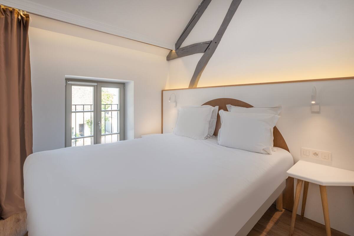 A bedroom with a large bed, a window, and a bedside table.