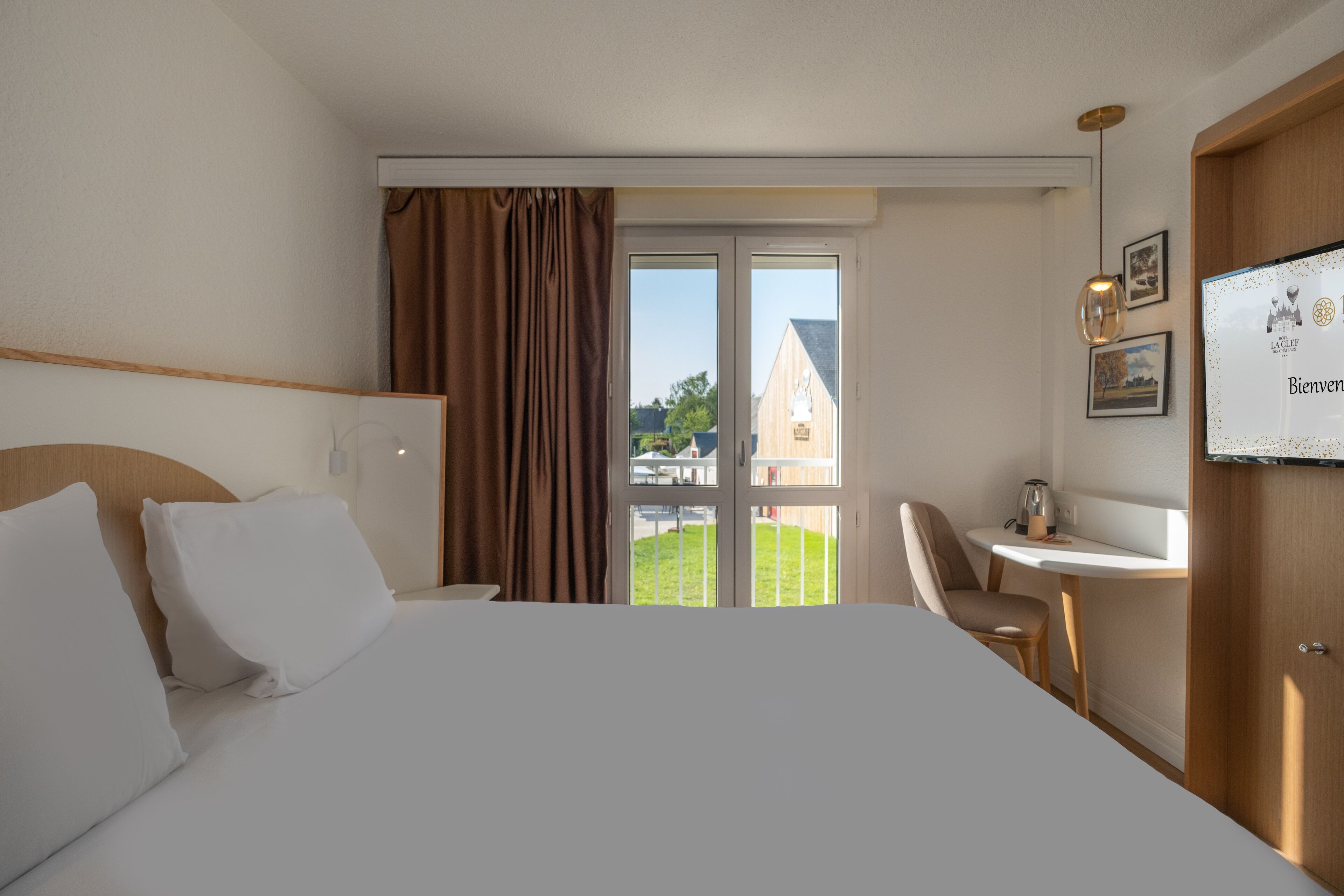 A hotel room with a large bed, a small table, a chair, and a view of a building through a glass door.