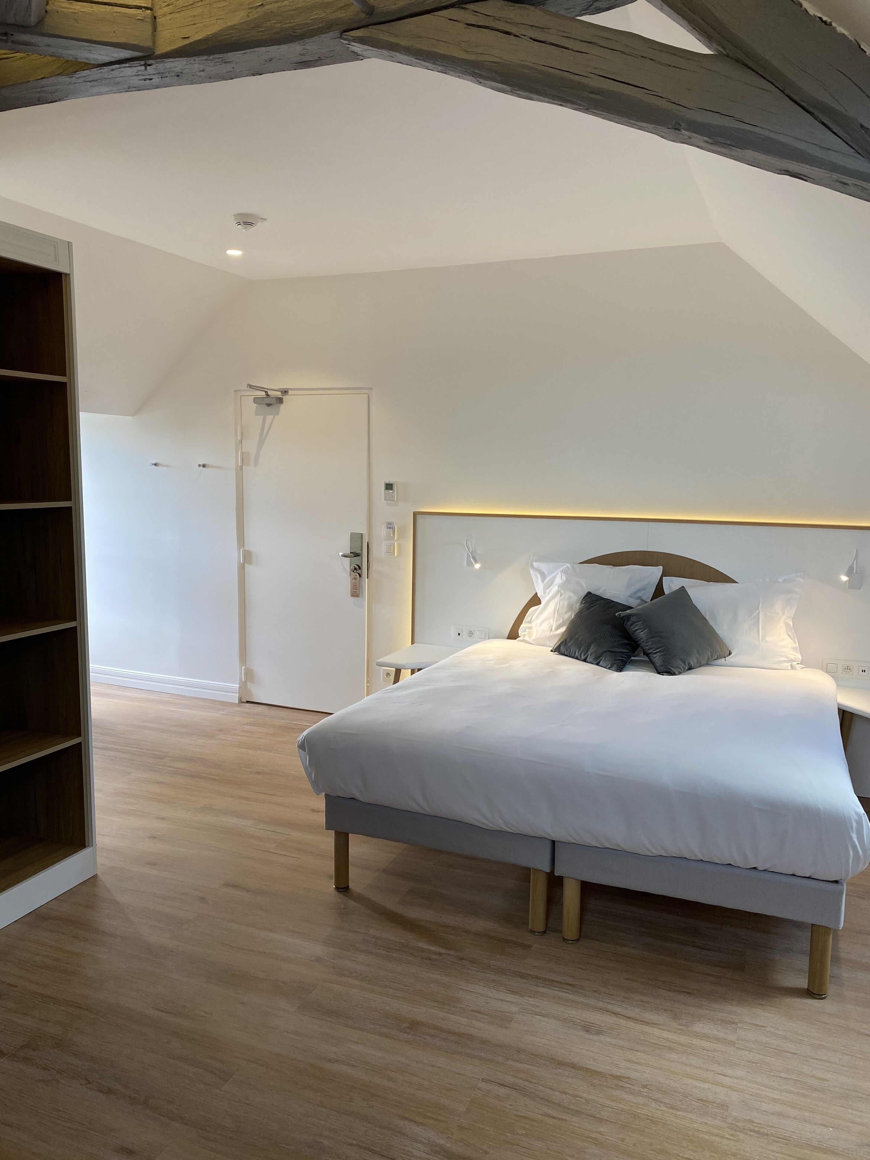 A bedroom with a bed, wooden floor, white walls, and a sloped ceiling.