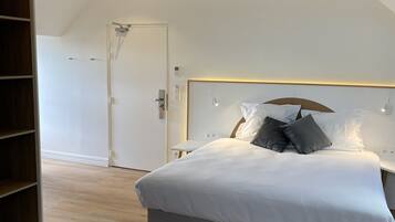 Een slaapkamer met een bed, houten vloer, witte muren en een schuine kap.