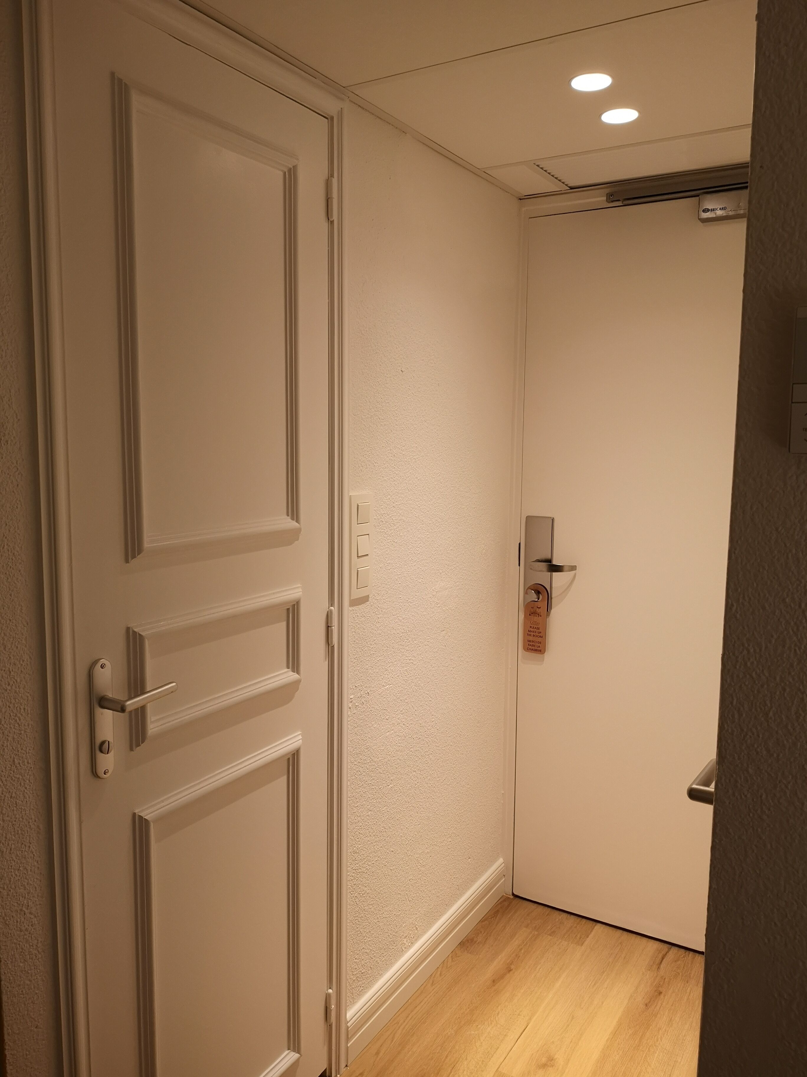 Una puerta cerrada con picaporte, un interruptor de luz y un termostato en la pared.