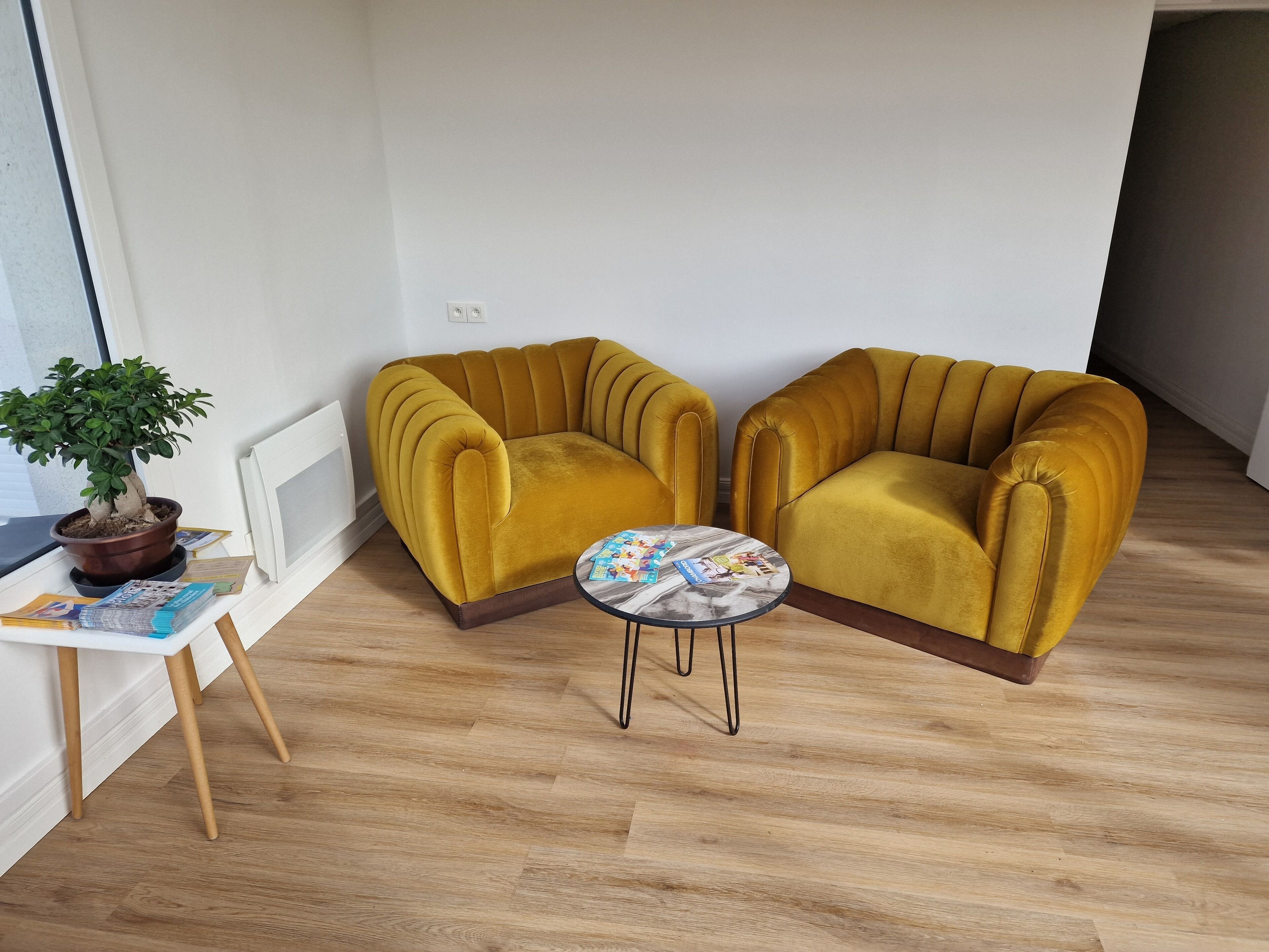Una habitación con dos sillones de color mostaza, una mesita redonda y una planta en maceta.