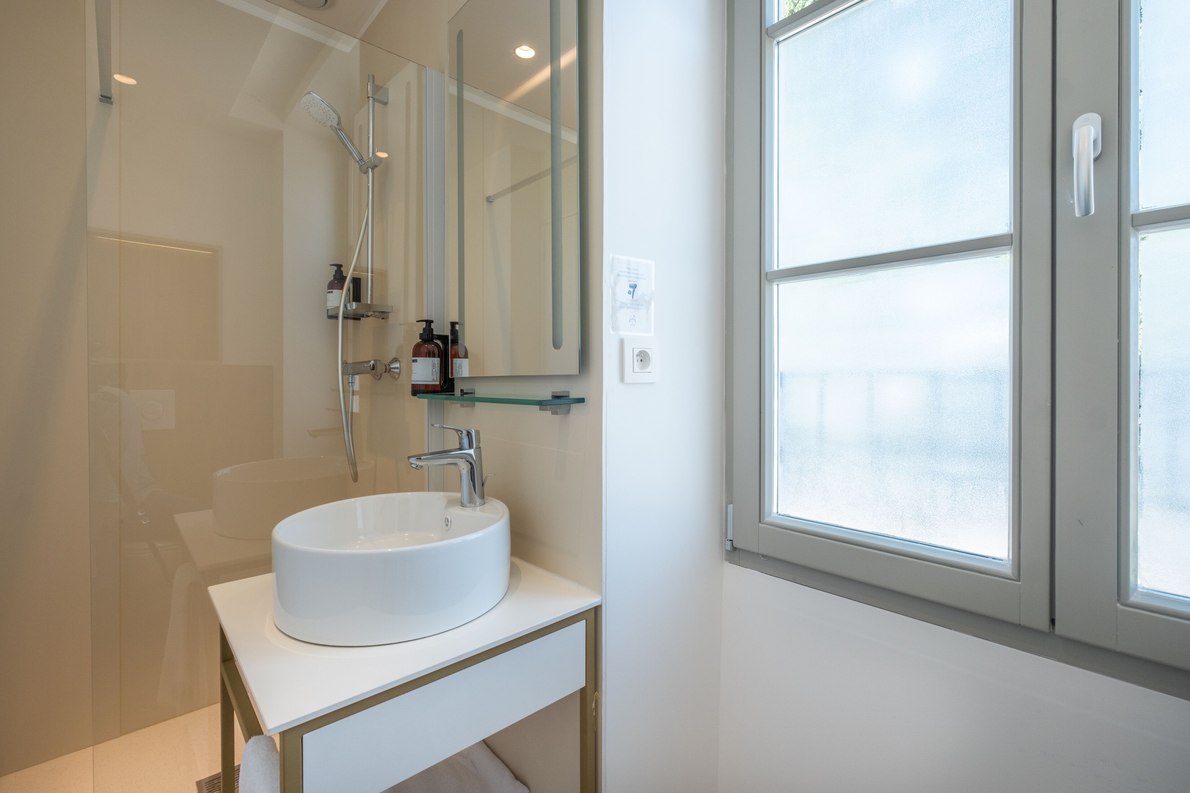 A modern bathroom with a white sink, a glass shower enclosure, and a large mirror.