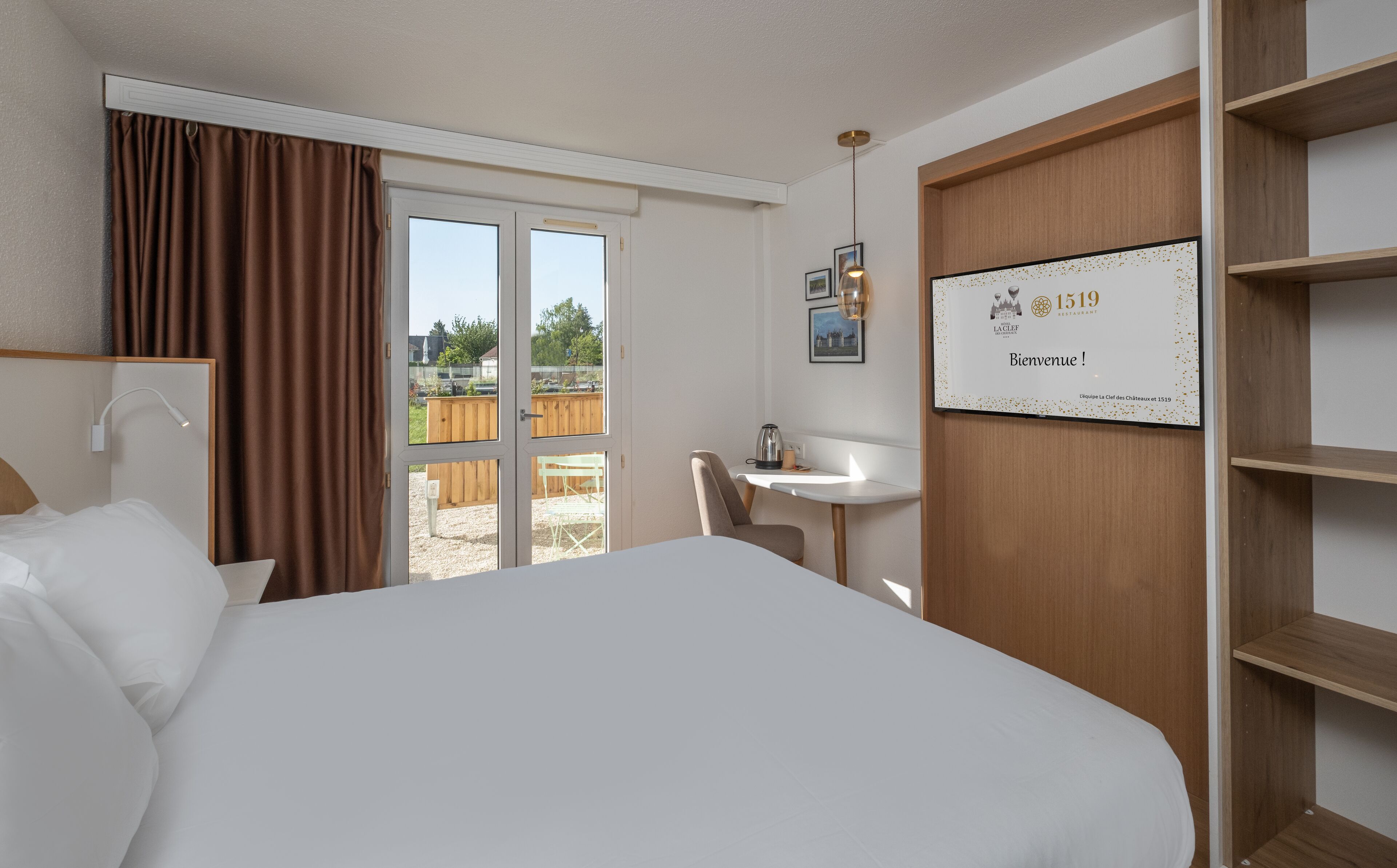 Een hotelkamer met een groot bed, een bureau, een stoel, een raam met gordijnen en een bord met een welkomstbericht aan de muur.