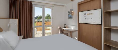 Een hotelkamer met een groot bed, een bureau, een stoel, een raam met gordijnen en een bord met een welkomstbericht aan de muur.