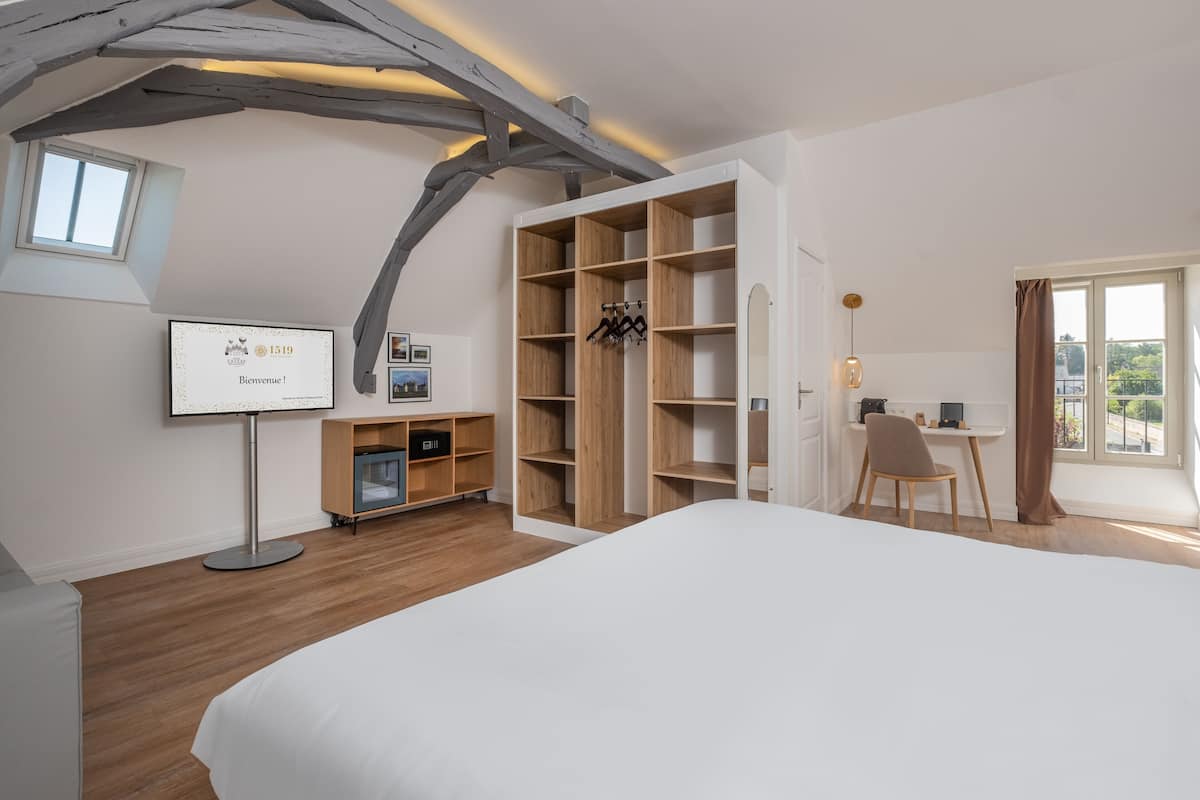 A modern hotel room with a large bed, wooden shelving, a desk, and a view of the outdoors.