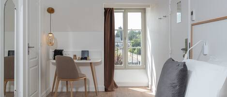 Ein Hotelzimmer mit Bett, Schreibtisch mit Computer, Stuhl, Fenster mit Vorhängen und Blick ins Freie.