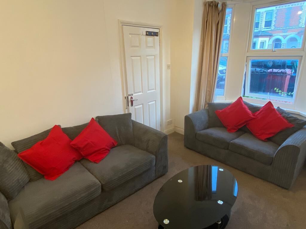 A living room with two grey sofas, each with red cushions, a black coffee table, a white door, and a window with curtains.