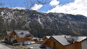 Una hilera de cabañas de madera con techos inclinados, con montañas nevadas y un cielo despejado al fondo.