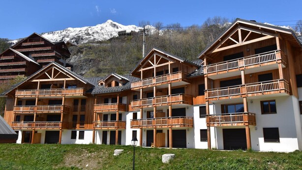 Una cabaña de madera de varios pisos con balcones, con montañas nevadas al fondo.