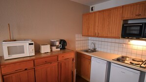 Cocina compacta con armarios de madera, microondas, tostadora, cafetera, lavabo y lavavajillas.