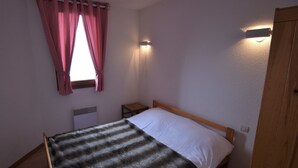 Un dormitorio pequeño y sencillo con una cama individual, una mesita de noche, un radiador y una ventana con cortinas.