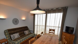 Una sala de estar acogedora con una mesa de comedor de madera, un sofá con cojines estampados, un reloj de pared y un televisor sobre un mueble de madera.
