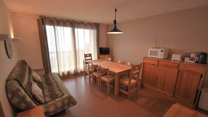 Una sala de estar acogedora con un sofá, una mesa de comedor con sillas, un televisor y una zona de cocina con microondas y armarios.
