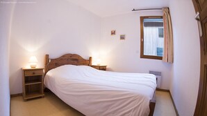 Un dormitorio con una cama de madera, dos mesitas de noche con lámparas, una ventana con cortinas y un radiador.