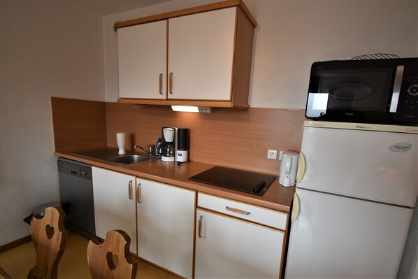 Una kitchenette compacta con microondas, cafetera y pequeño refrigerador.