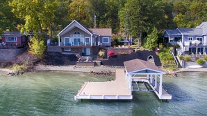 A lakeside property with a dock, a large house with a deck, and a smaller house with a balcony. - Just Bluffin': Keuka Lake Luxury Rental + Hot Tub! Close to Wineries (Penn Yan)