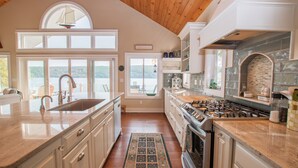 A spacious kitchen with a large island, a stove, and a view of the lake. - Just Bluffin': Keuka Lake Luxury Rental + Hot Tub! Close to Wineries (Penn Yan)