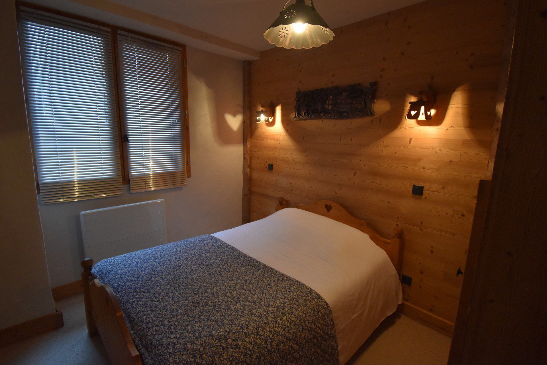 Une chambre à coucher avec une tête de lit en bois, un lit recouvert d’une couette blanche et deux lampes fixées au mur.