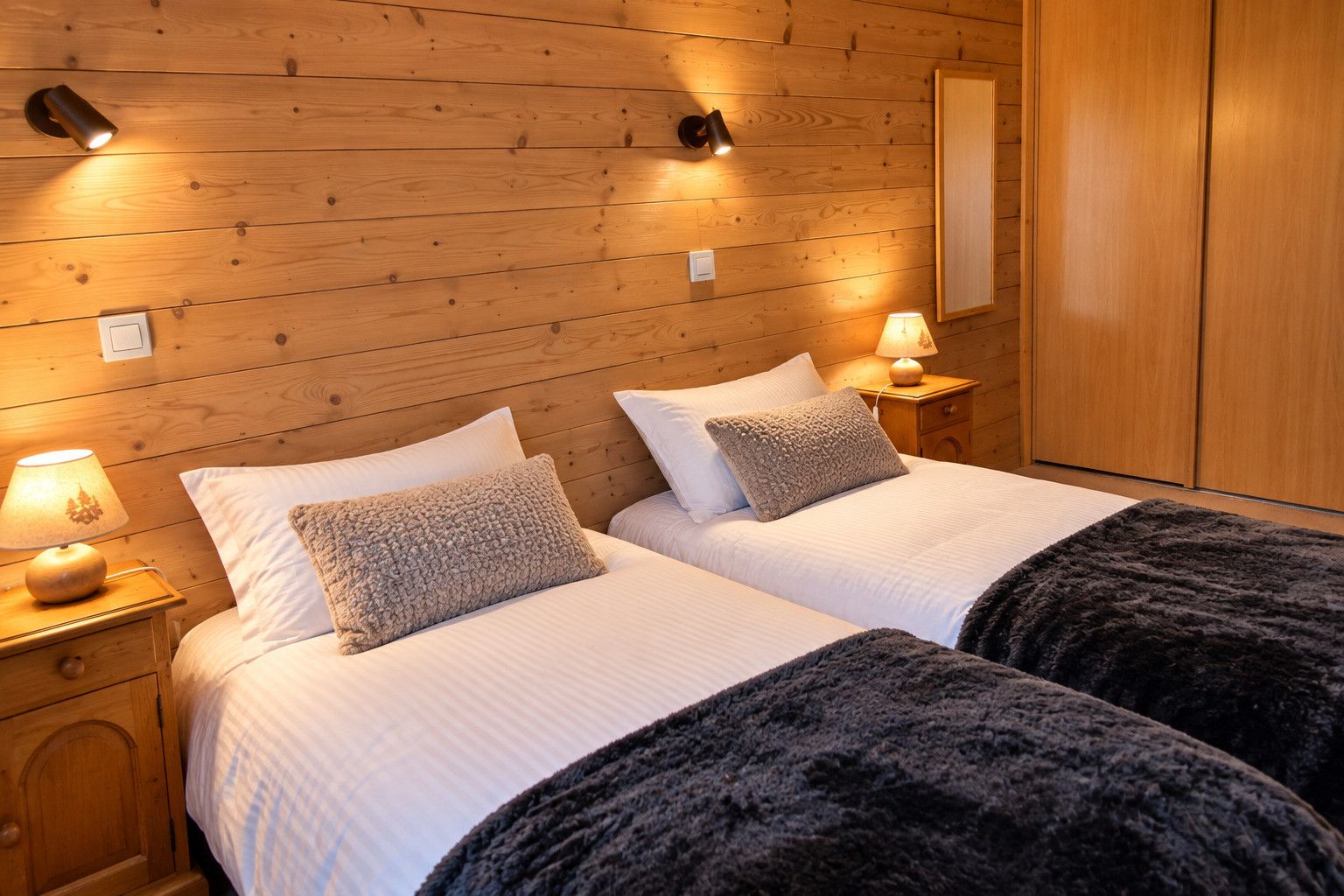 Una habitación doble con paredes de madera, dos camas con ropa blanca, lámparas de noche y un armario.