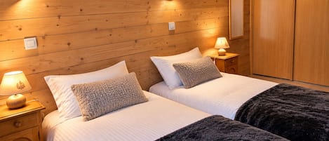 A double room with wooden walls, two beds with white bedding, bedside lamps, and a wardrobe.