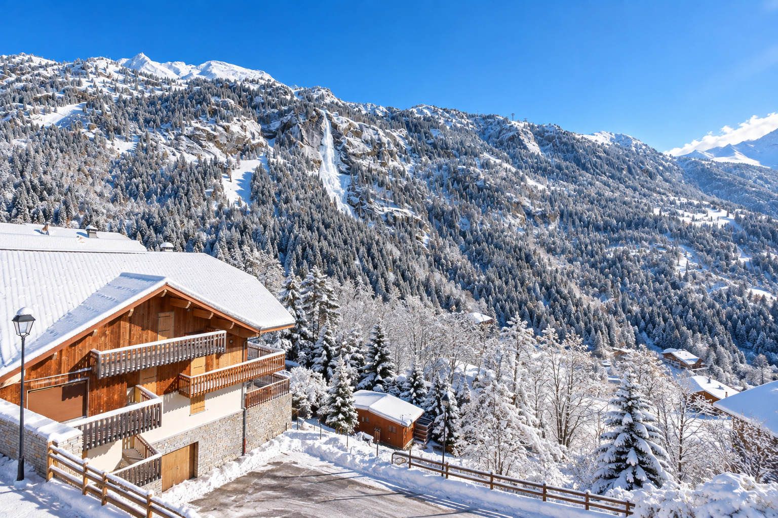 A wooden chalet with a balcony, surrounded by snow-covered trees and mountains.