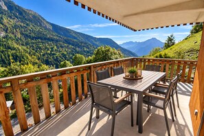 A wooden deck with a table and chairs, overlooking a mountainous landscape.