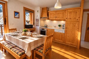 A cozy kitchen with wooden cabinets, a dining table set for four, and a view of a snowy landscape through the window.