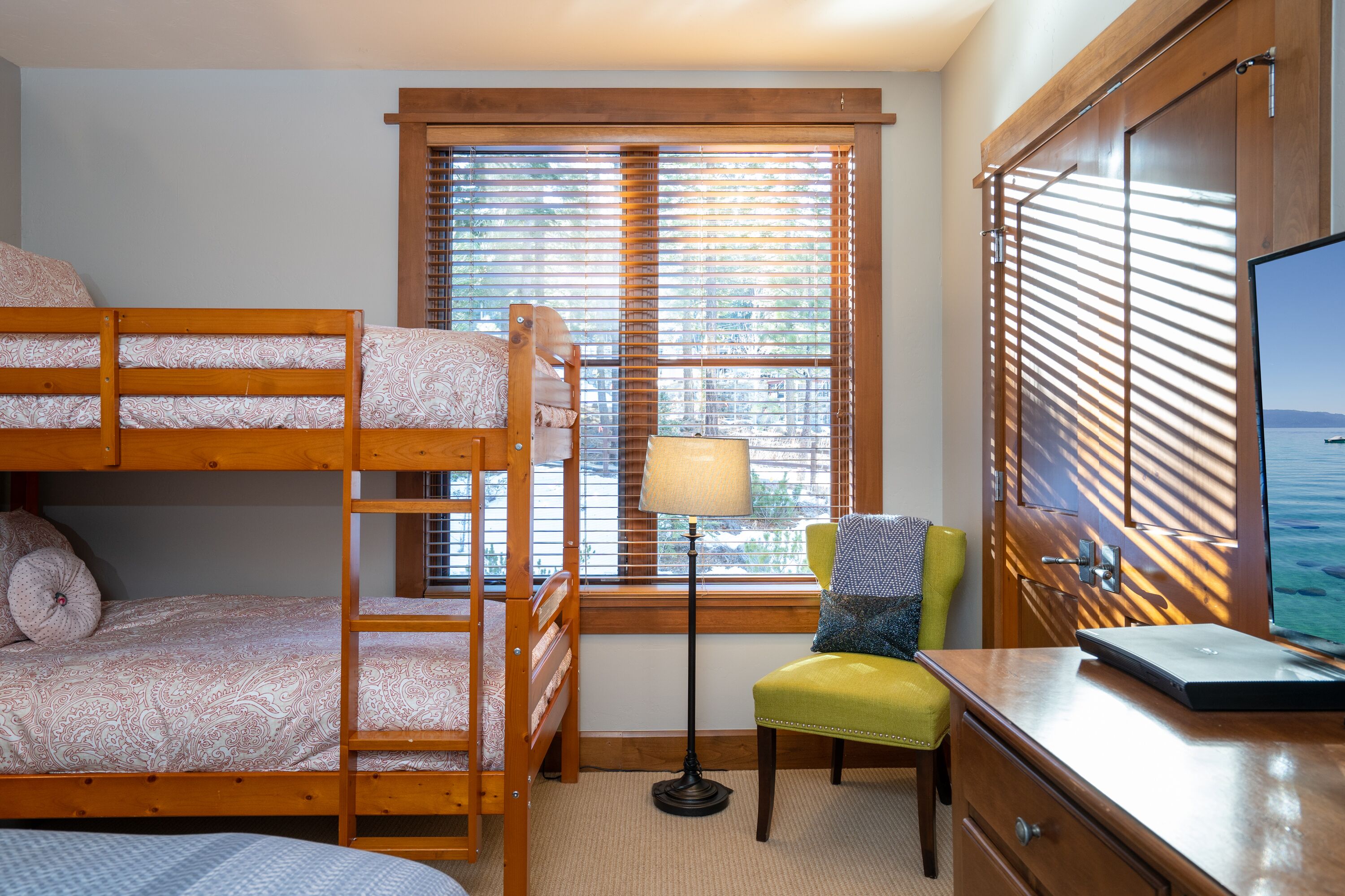 Una cama litera con escritorio y silla, una lámpara y una ventana con persianas.