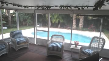 Une terrasse couverte avec des fauteuils en osier, une petite table et une vue sur une piscine.