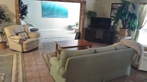 A living room with a sofa, armchair, coffee table, and a TV stand. - Comfortable 3 bedroom 3 bath beach house .pool..3 minute walk to beach. (Vero Beach)