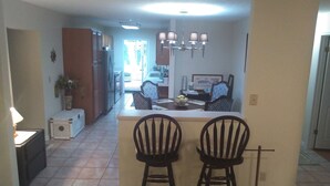 A kitchen with a central island, two bar stools, a chandelier, and a dining area with patterned chairs. - Comfortable 3 bedroom 3 bath beach house .pool..3 minute walk to beach. (Vero Beach)