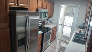 A kitchen with wooden cabinets, stainless steel appliances, and a tiled floor. - Comfortable 3 bedroom 3 bath beach house .pool..3 minute walk to beach. (Vero Beach)