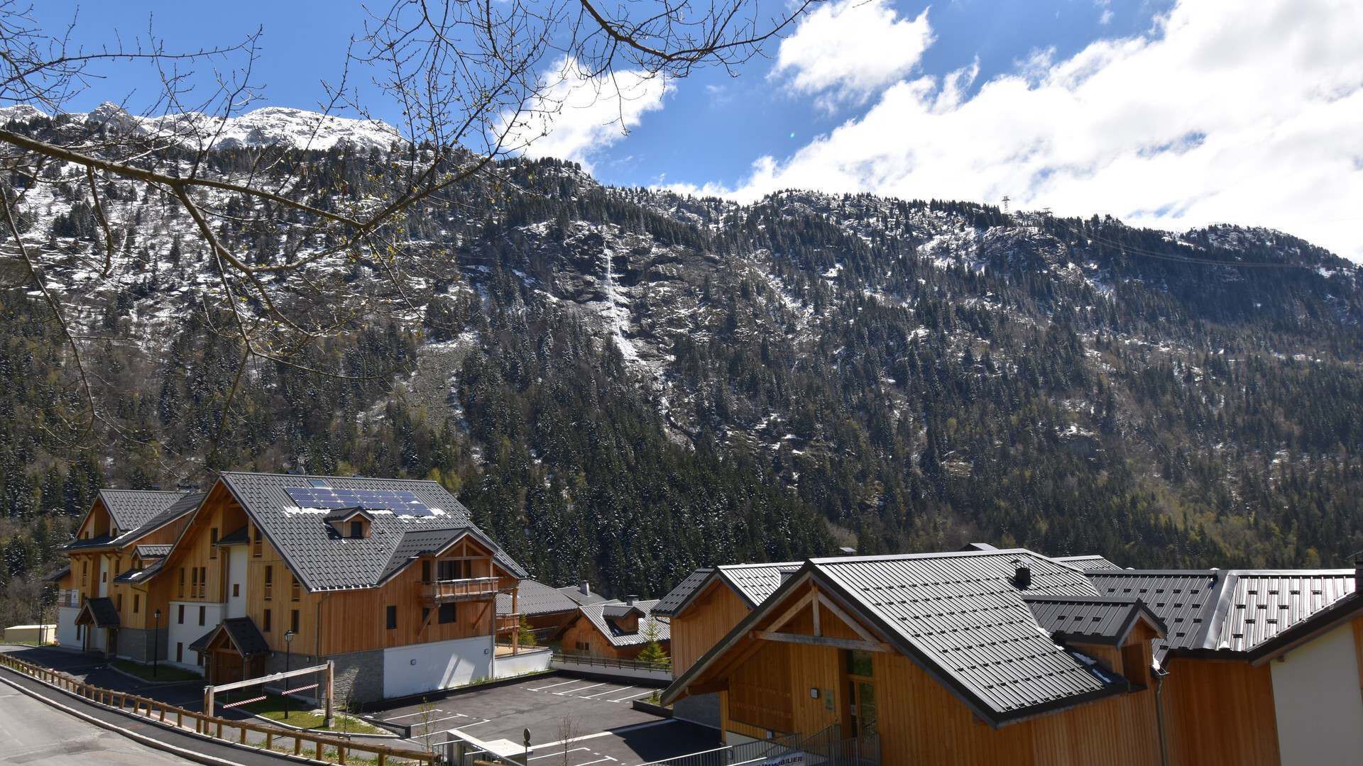 A row of wooden cabins with sloped roofs, set against a backdrop of snow-capped mountains and a clear sky.