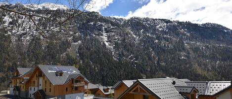 A row of wooden cabins with sloped roofs, set against a backdrop of snow-capped mountains and a clear sky.