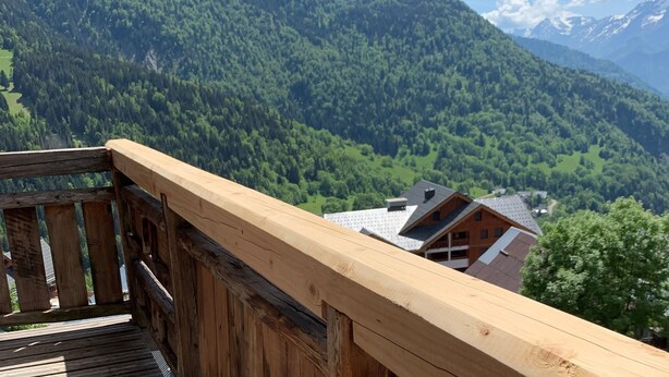 A wooden deck overlooking a mountainous landscape with a view of a building with a sloped roof. - Les Cimes - Five Bedroom Apartment, Sleeps 10 (Vaujany)
